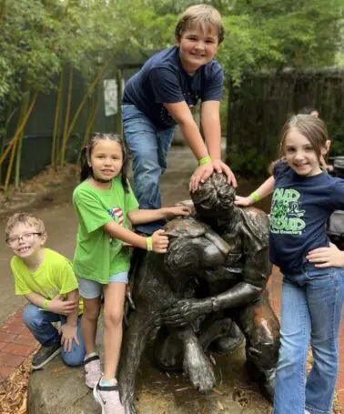 A group of children standing around a statue.