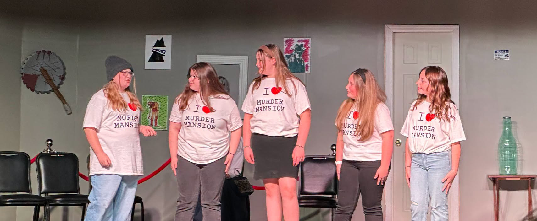 Student performers stand together on stage wearing production shirts.